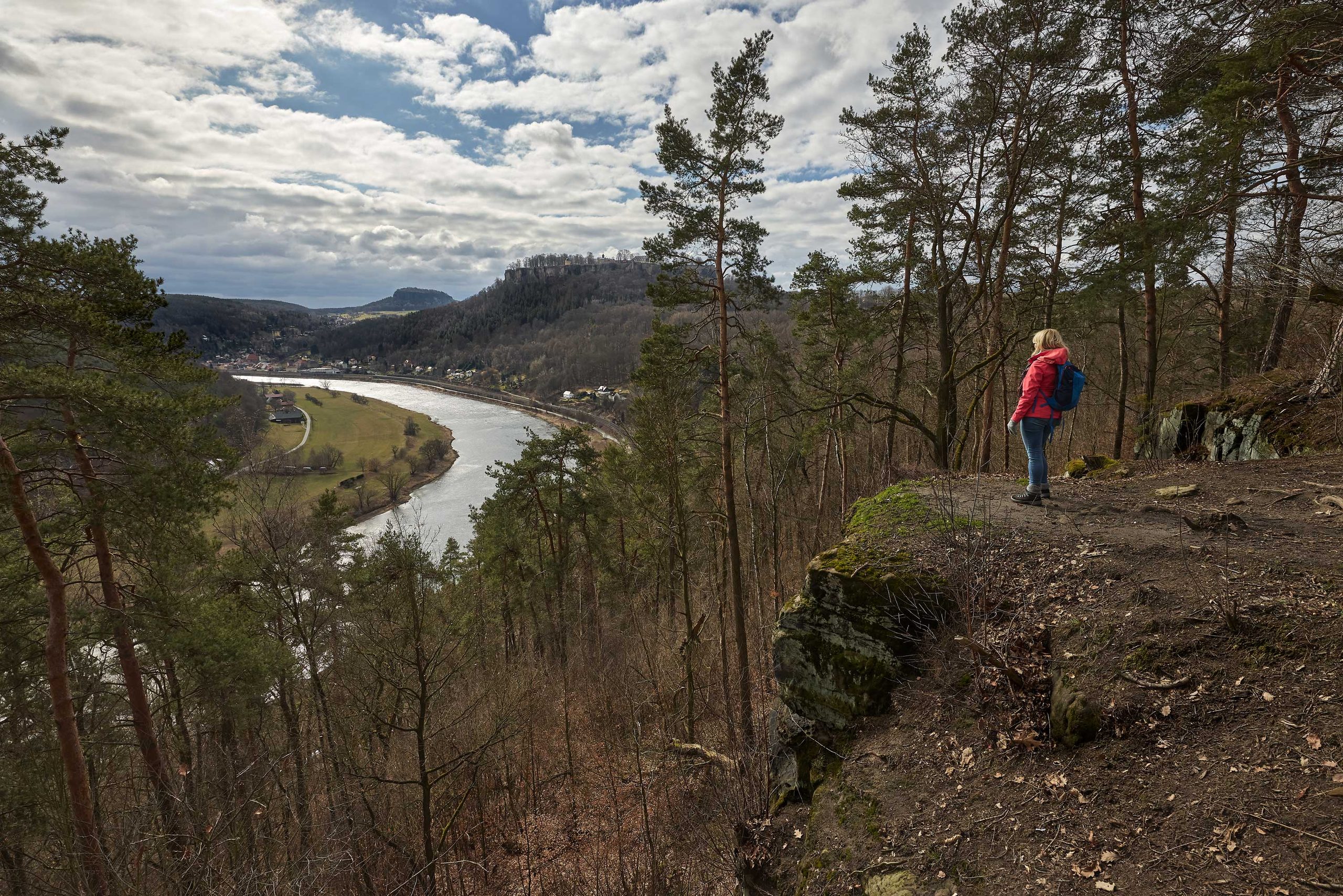 Ein Wanderer mit Rucksack steht auf einer Klippe und blickt auf einen Fluss, der sich durch ein Tal schlängelt.