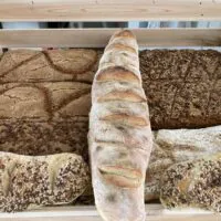 Eine Holzkiste, gefüllt mit verschiedenen Brotsorten, darunter Körnerbrot, knuspriges Brot und rustikales Brot, die ordentlich nebeneinander angeordnet sind.