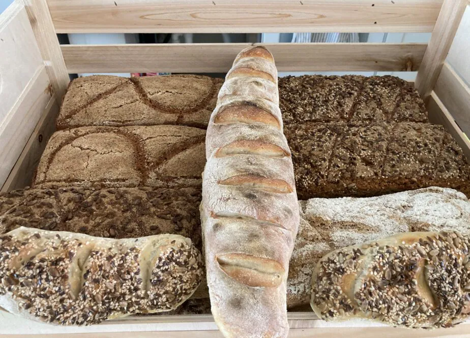 Eine Holzkiste, gefüllt mit verschiedenen Brotsorten, darunter Körnerbrot, knuspriges Brot und rustikales Brot, die ordentlich nebeneinander angeordnet sind.
